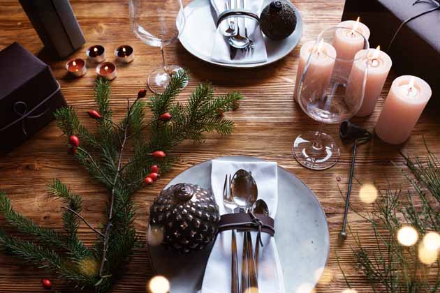 Ein winterlich gedeckter Holztisch mit Geschirr und Besteck, Kerzen, Teelichtern, Tannenzweigen und Geschenken.